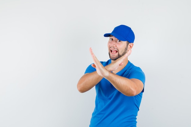 Young male showing refusal gesture in blue t-shirt and cap and looking happy