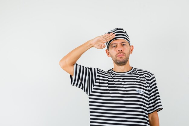 Young male showing salute gesture in striped t-shirt hat and looking confident  