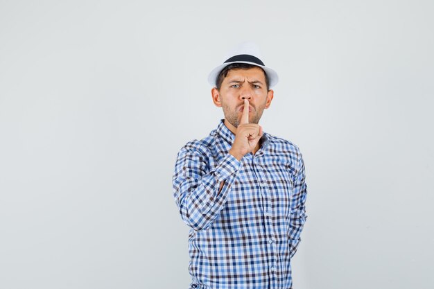 Young male showing silence gesture in checked shirt