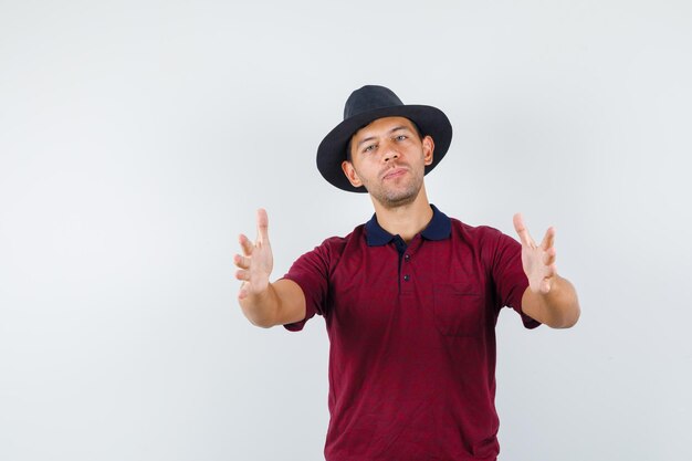 Young male showing size sign or holding something in t-shirt, hat front view.