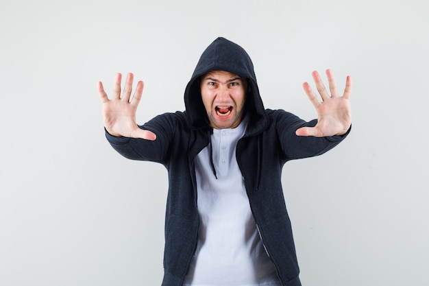 Young male showing stop gesture by screaming in t-shirt, jacket and looking agitated. front view.