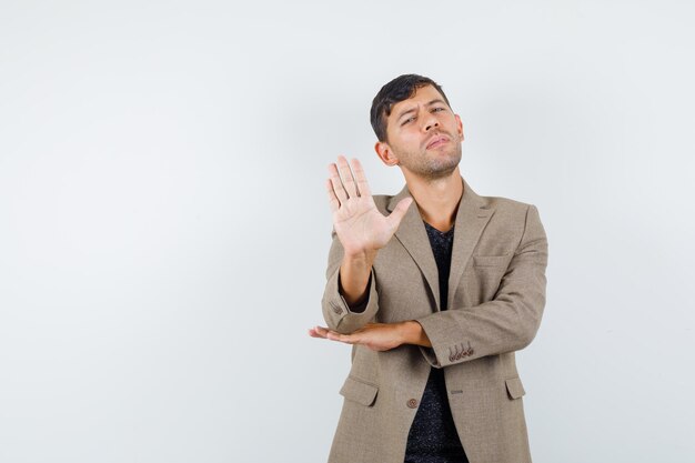 Young male showing stop gesture in grayish brown jacket,black shirt and looking serious. front view. free space for your text