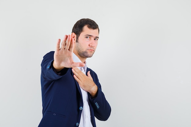 Young male showing stop gesture in shirt, jacket and looking serious