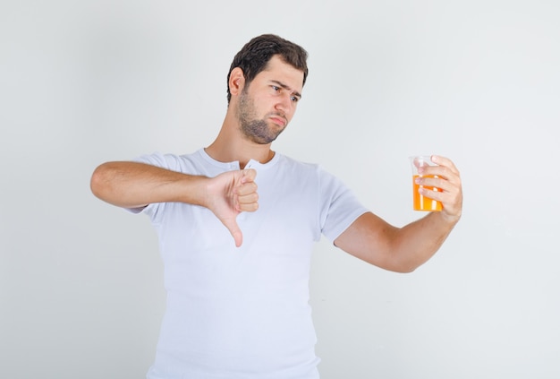 Young male showing thumb down with juice in white t-shirt and looking dissatisfied.