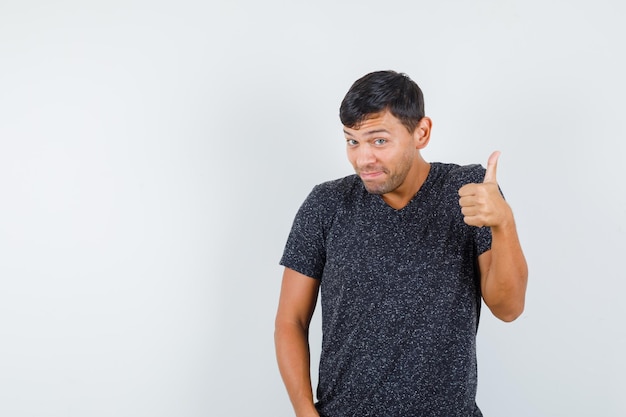 Young male showing thumb up in black t-shirt and looking satisfied , front view. space for text