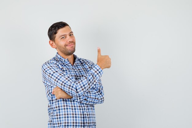 Young male showing thumb up in checked shirt and looking merry