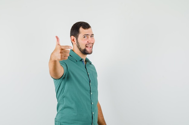 Giovane maschio che mostra pollice in su in camicia verde e sembra felice. vista frontale.