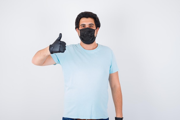 Young male showing thumb up in t-shirt and looking confident. front view.