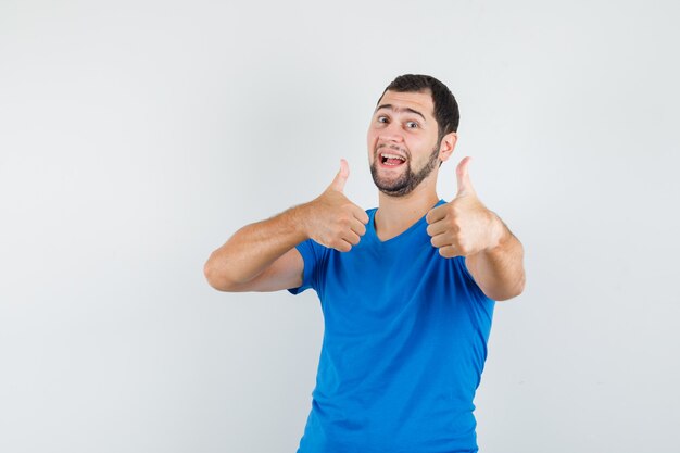 Молодой мужчина показывает палец вверх в синей футболке и выглядит весело