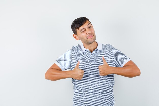 Молодой мужчина показывает палец вверх в футболке и выглядит радостным
