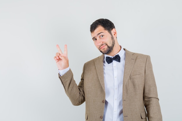 Young male showing victory sign in suit and looking confident. front view.