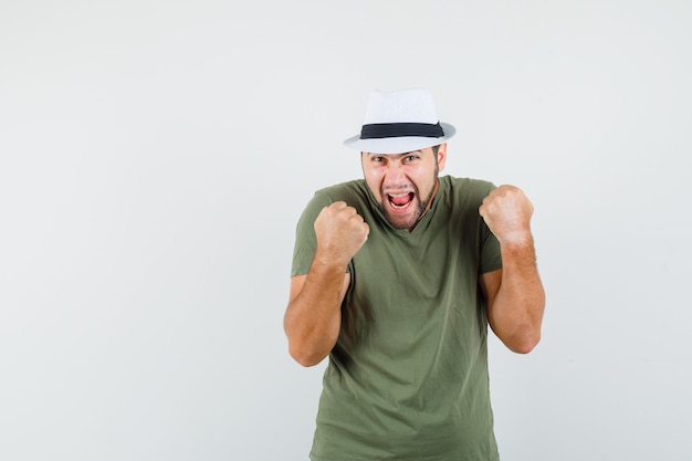 Young male showing winner gesture in green t-shirt and hat and looking blissful