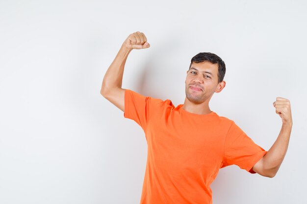 オレンジ色のTシャツで勝者のジェスチャーを示し、幸せそうに見える若い男性