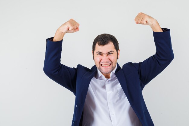 Young male showing winner gesture in shirt, jacket and looking blissful