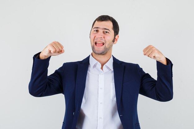 Young male showing winner gesture in shirt and jacket and looking blissful