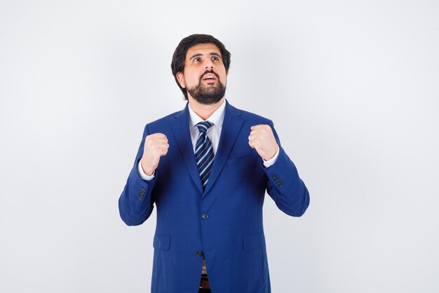 Young male showing winner gesture in shirt,jacket,tie , front view.