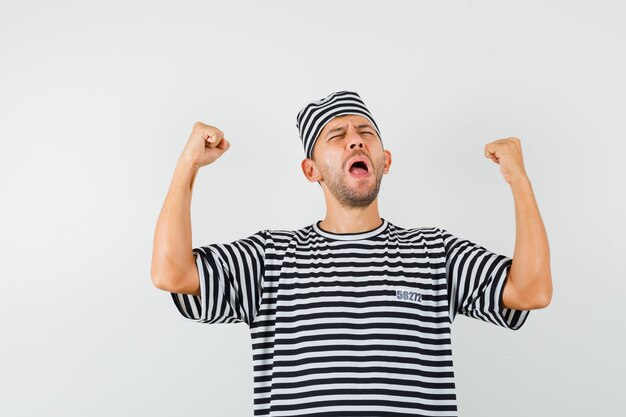 Young male showing winner gesture in striped t-shirt hat and looking happy  