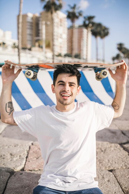 Young male skateboarder holding skateboard on his head