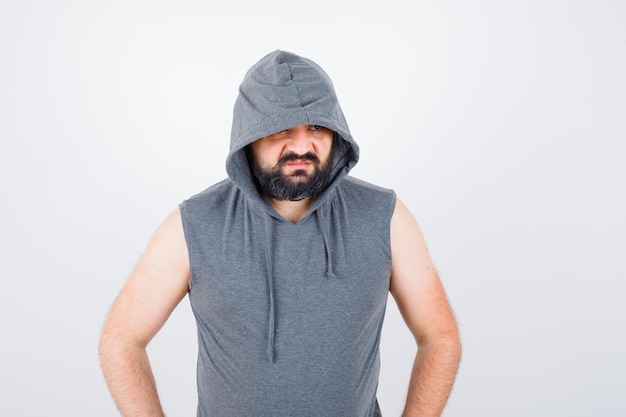 Free photo young male in sleeveless hoodie, cap looking away and looking confident , front view.