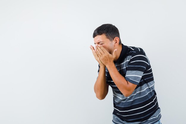 Young male sneezing and having flu in t-shirt and looking sick. front view.