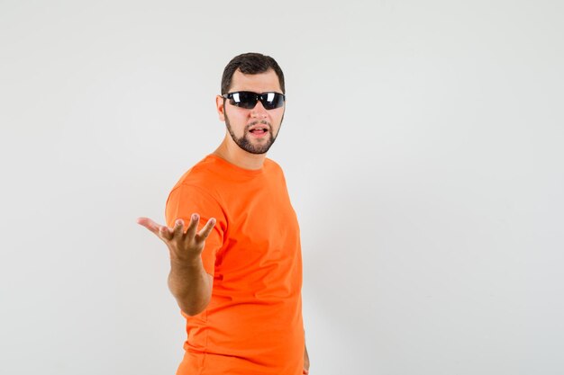 Young male spreading hand showing puzzled gesture in orange t-shirt , front view.