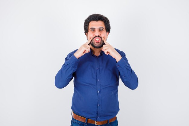 Young male squeezing his cheeks with fingers in royal blue shirt front view.