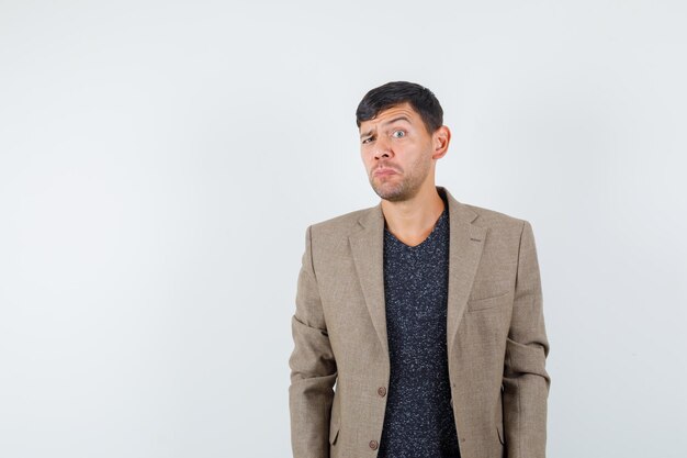 Young male standing calmly in grayish brown jacket,black shirt and looking doubtful , front view. space for text