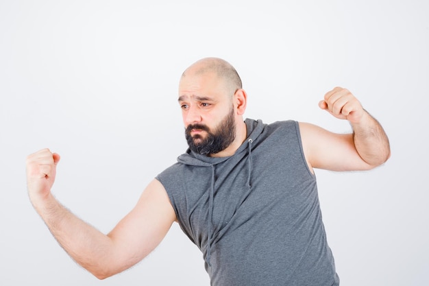 Free photo young male standing in fight pose in sleeveless hoodie and looking spiteful. front view.