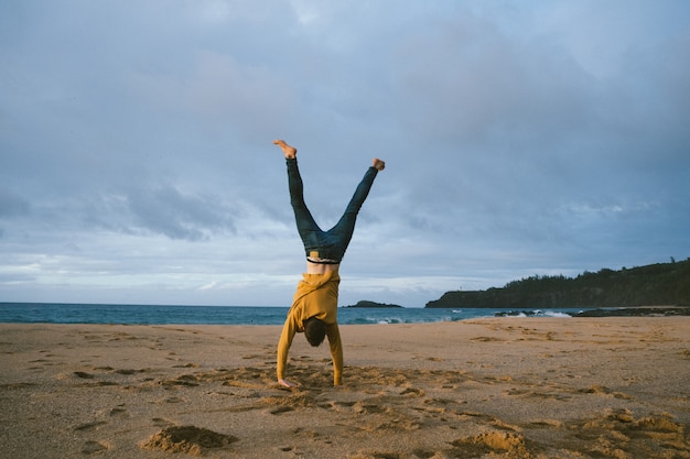 Young male standing on his arms at the sandy beach on a sunny day