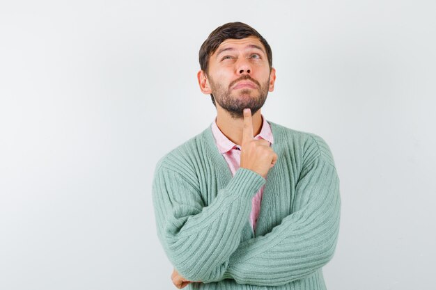 Young male standing in thinking pose in shirt, cardigan and looking pensive. front view.