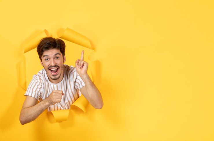 मुफ़्त फोटो young male standing on torn yellow paper background guy indoor sale facial