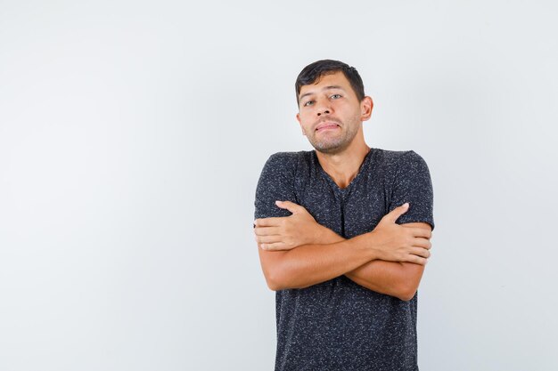 Young male standing with crossed arms in black t-shirt and looking frozen. front view. space for text