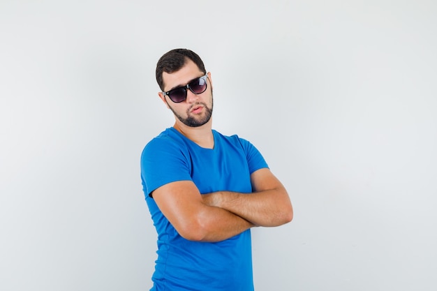 Free photo young male standing with crossed arms in blue t-shirt and looking cool