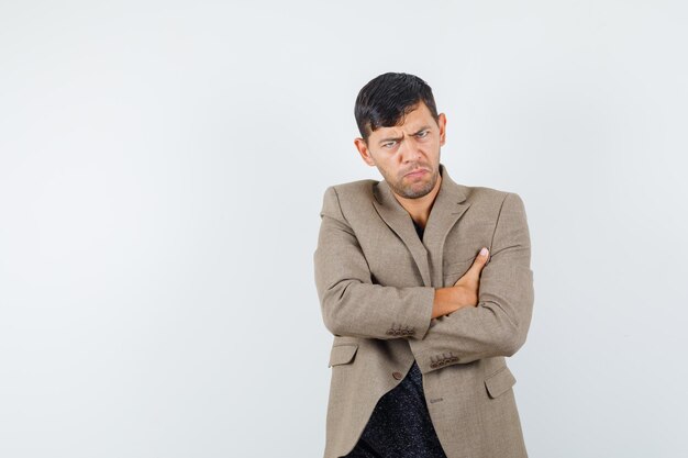 Young male standing with crossed arms in grayish brown jacket,black shirt and looking offended , front view. free space for your text