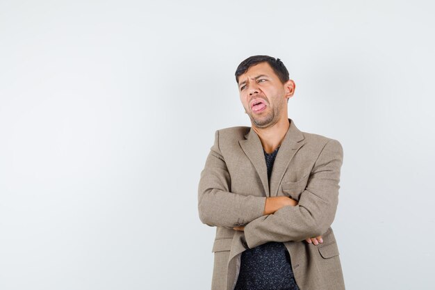 Young male standing with crossed arms in grayish brown jacket and looking disgusted. front view. space for text