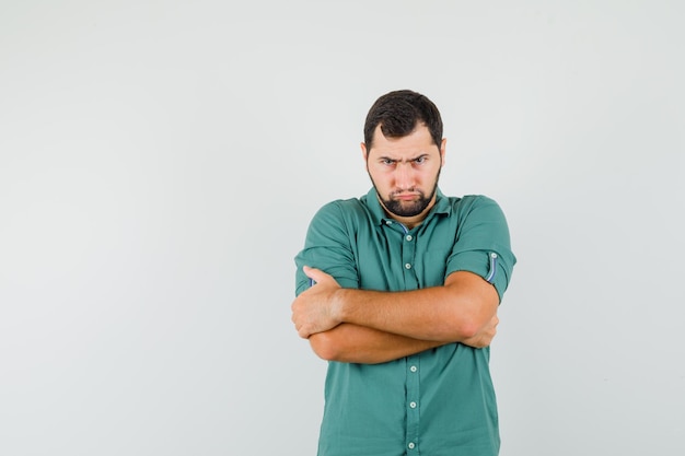 Young male standing with crossed arms in green shirt and looking offended. front view. space for text