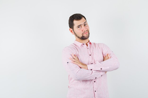 Young male standing with crossed arms in pink shirt and looking sensible