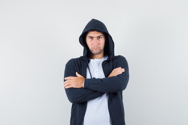 Young male standing with crossed arms in t-shirt, jacket and looking serious , front view.