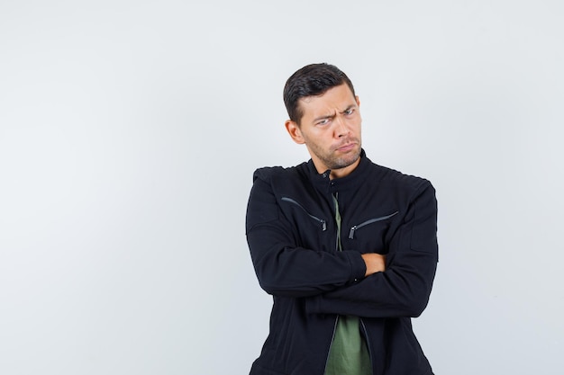 Young male standing with crossed arms in t-shirt, jacket and looking strict , front view.