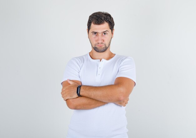 Young male standing with crossed arms in white t-shirt and looking pensive