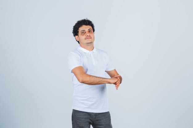 Young male standing with open palm stopping clenched fist in white t-shirt, pants and looking confident. front view.