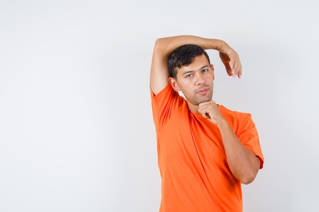 Young male stretching arm in orange t-shirt and looking thoughtful