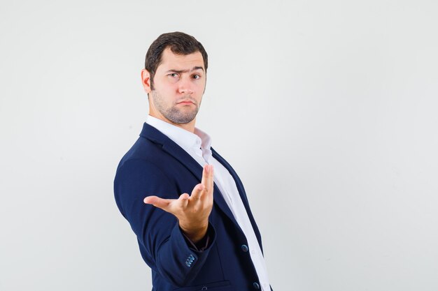 Young male stretching hand in puzzled gesture in shirt and jacket