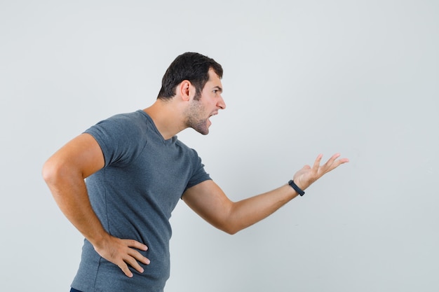 Young male stretching hand in questioning manner in grey t-shirt and looking angry  