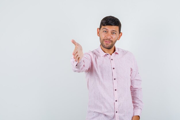 Young male stretching out hand for shaking in pink shirt front view.