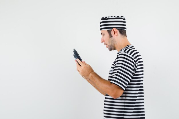 Young male in striped t-shirt,cap looking at clock and looking focused .