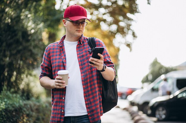 公園で携帯電話を使用してコーヒーを飲む若い男性学生