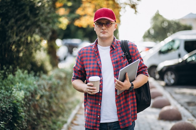 Young male student drinking coffee with laptop in park