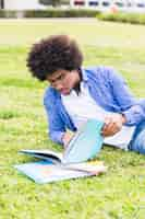 Free photo young male student leaning on lawn reading the book