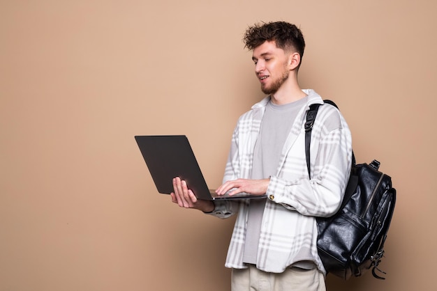 Young Male student with modern laptop on color background